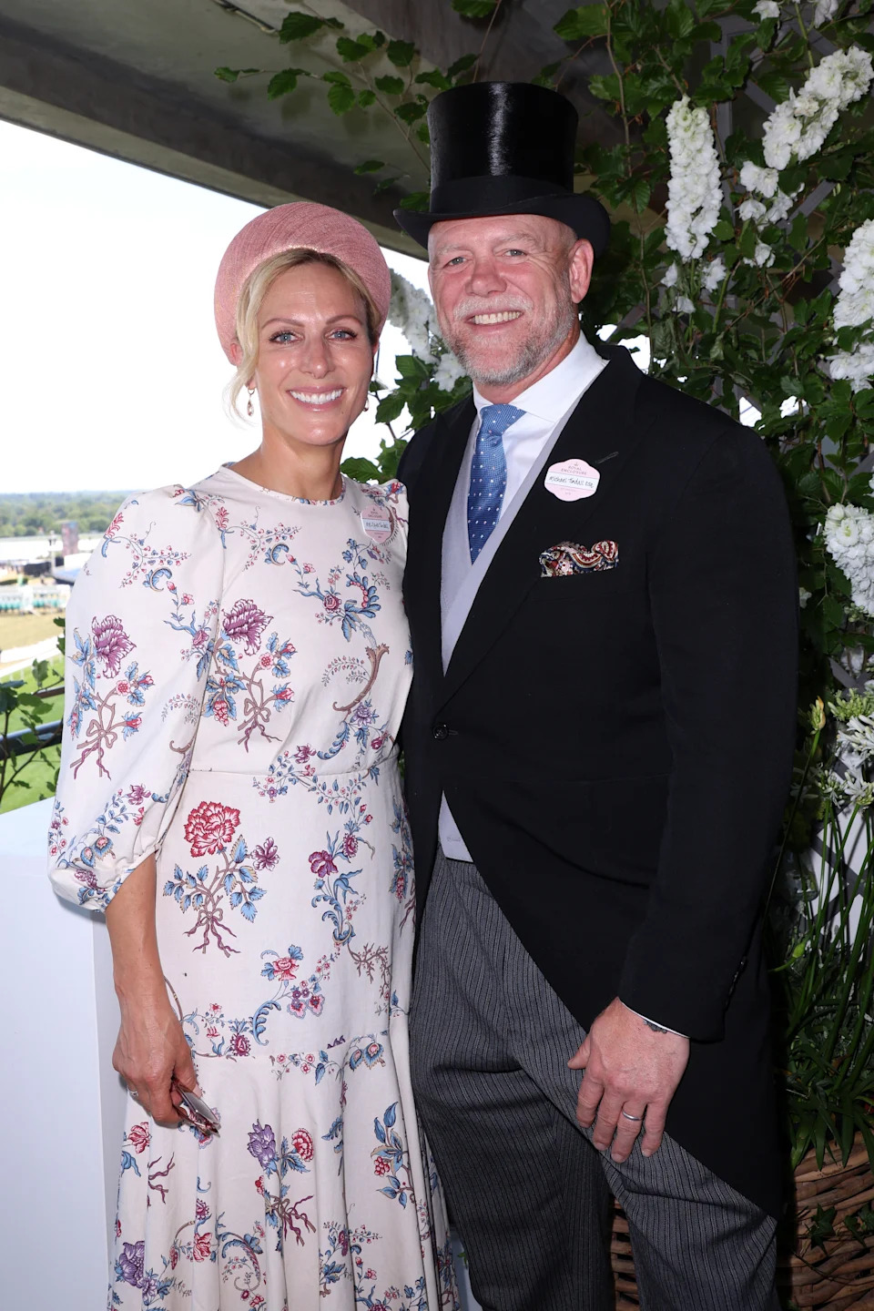 Zara Tindall wearing a white floral dress and pink headband standing with Mike Tindall, dressed in a top hat and suit