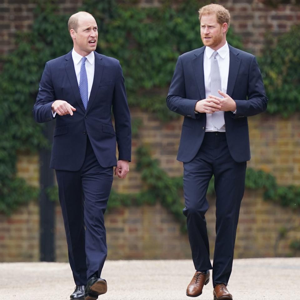Prince Harry and Prince William walking next to each other in blue suits .