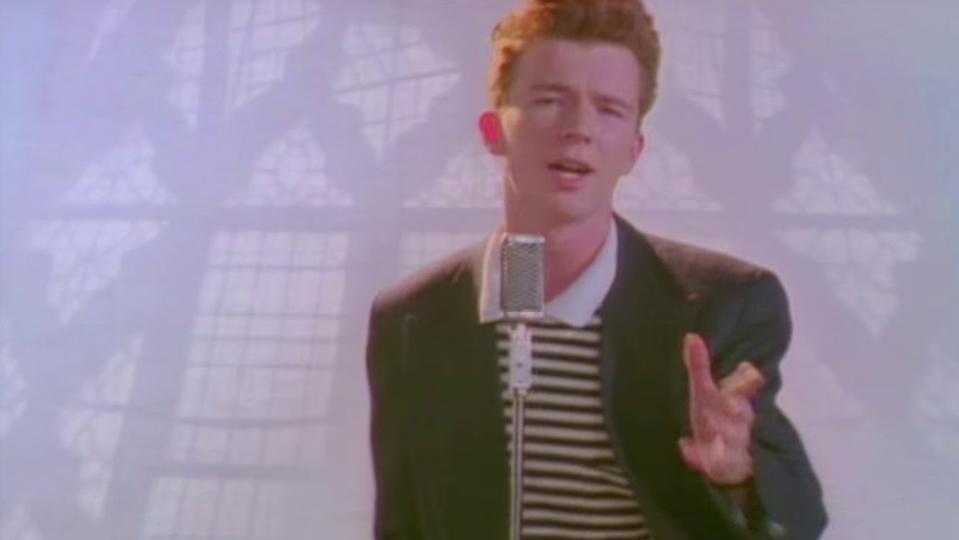 Person singing into a vintage microphone, wearing a striped shirt and blazer, in a softly lit setting with window patterns in the background