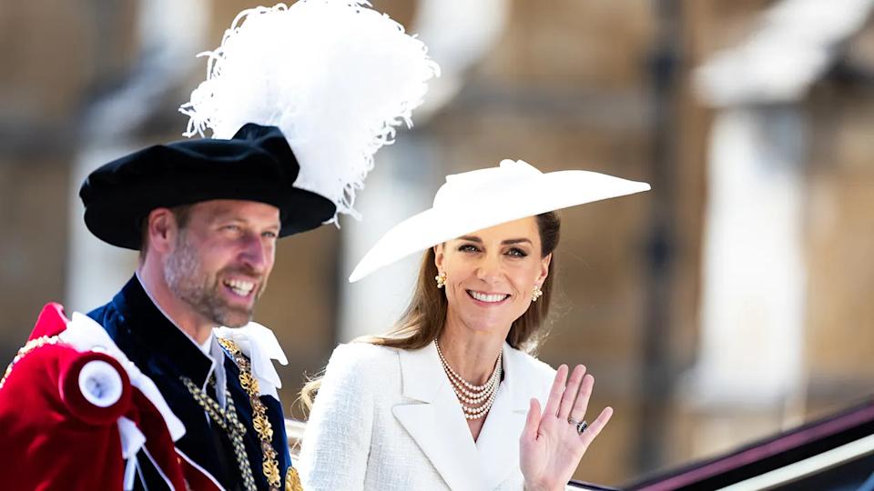 Prince William and Kate Middleton in formal royal attire sitting on a carriage smiling and waving to the public.