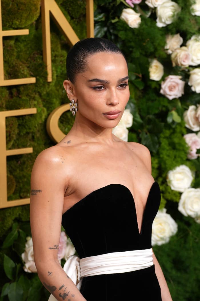 Zoë Kravitz in a strapless black gown with a white belt stands on a floral backdrop, exuding elegance