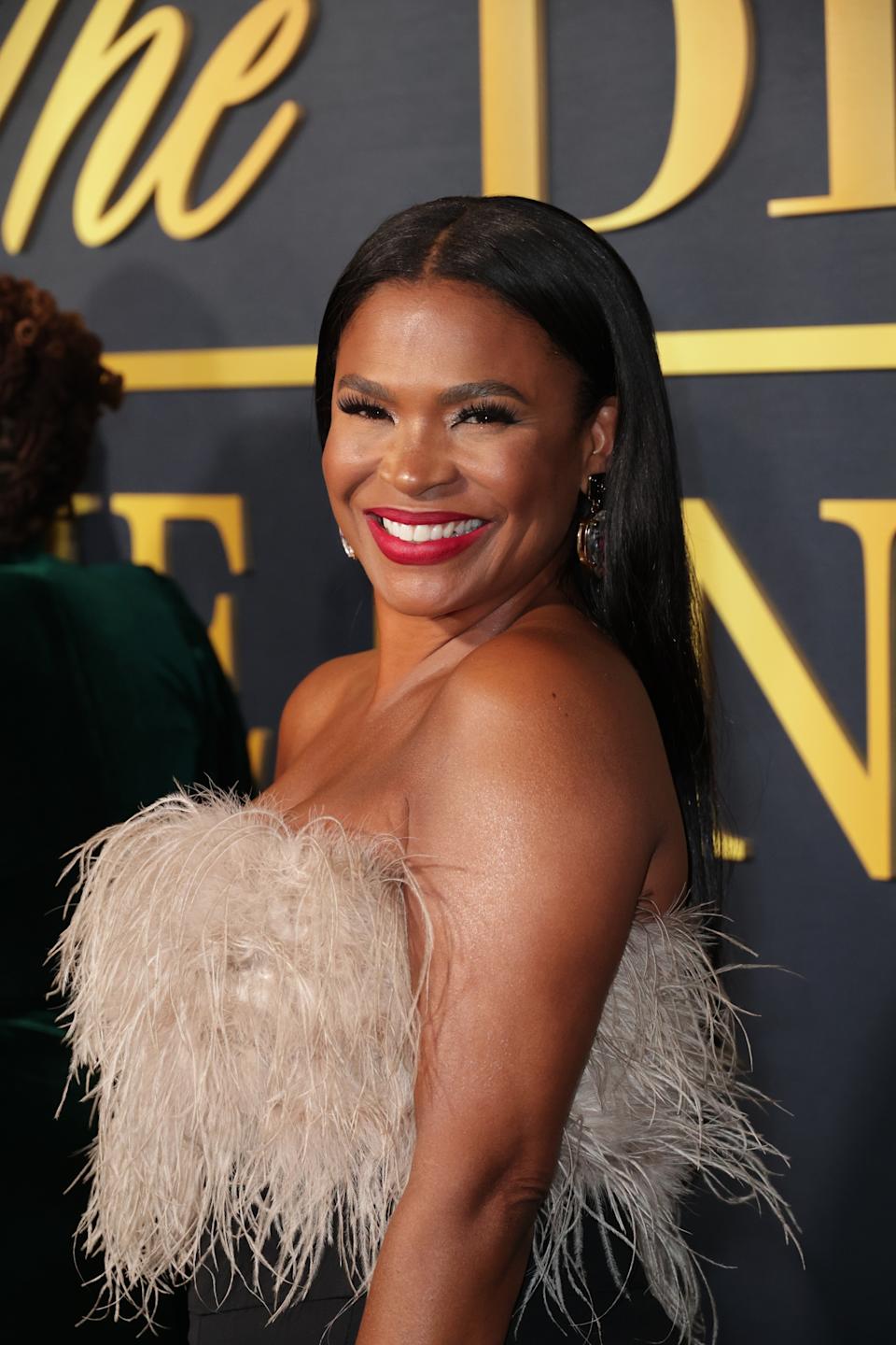 Nia Long smiling on the red carpet, wearing a strapless dress with feather detailing