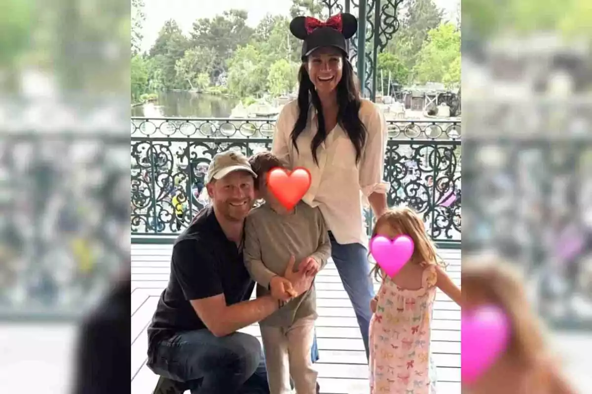 Meghan Markle and Prince Harry's family poses at a Disney's theme park, Meghan is wearing a cap with mouse ears, and the children's faces are covered with colorful hearts.