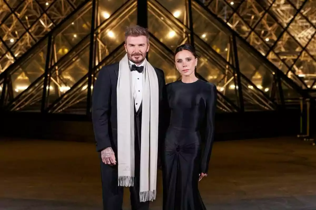 Two elegantly dressed people pose in front of an illuminated glass structure. Two elegantly dressed people pose in front of an illuminated glass structure.