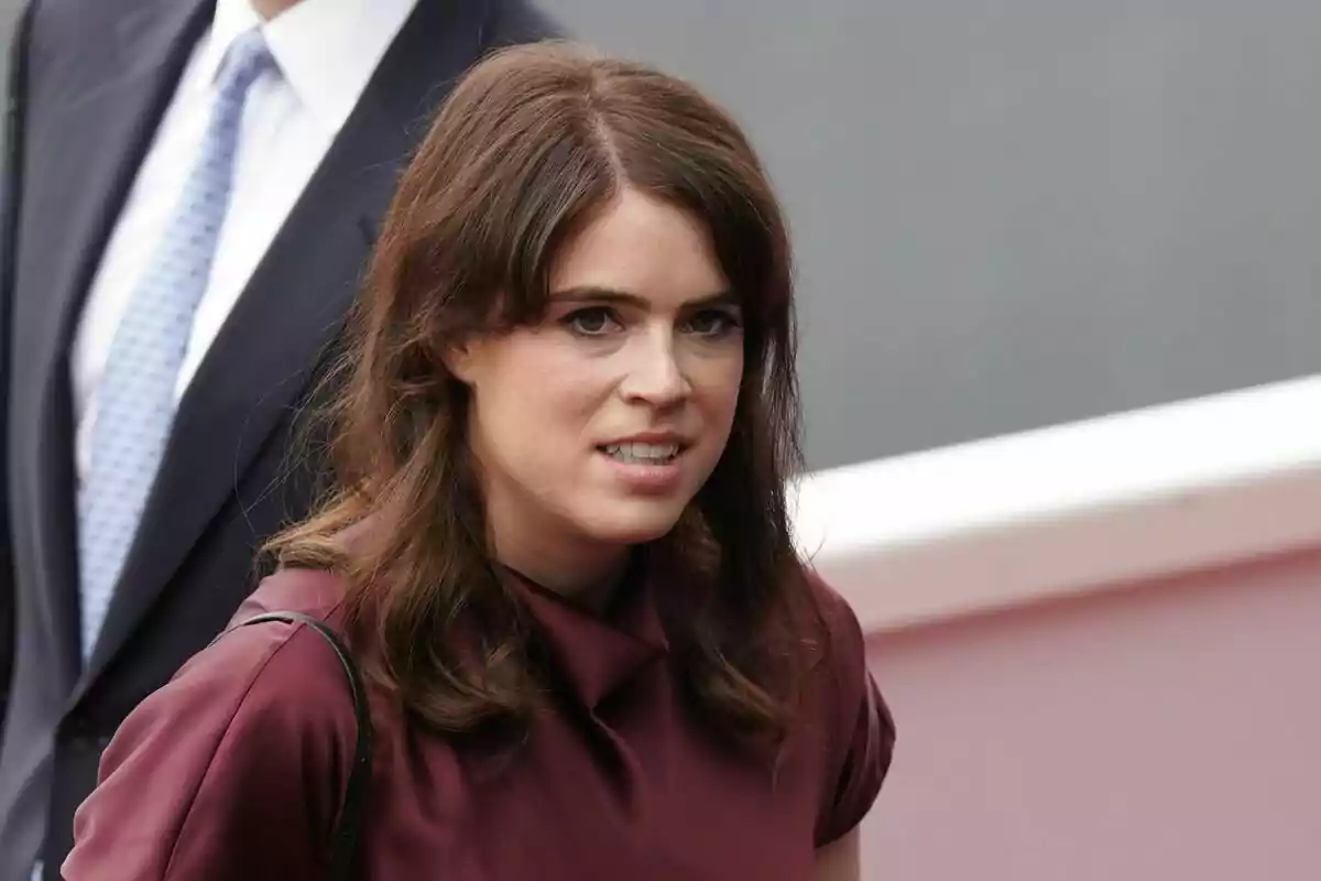 Brown-haired woman with loose hair wearing a burgundy blouse, walking outdoors next to a person in a dark suit