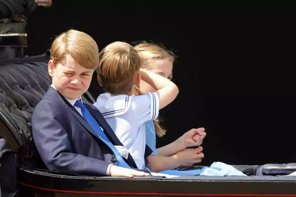 Boy in a blue suit winking while riding in a carriage with two other children