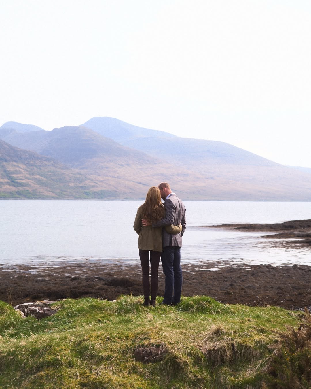 Prince William and Kate Middleton putting their arms around each other in Scotland facing a mountain