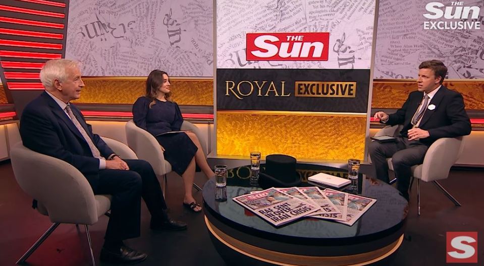 Three people sitting on a talk show set, discussing a newspaper article.