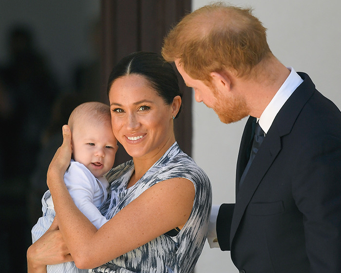 Meghan Markle holding her child while Prince Harry looks on during a public event with family focus. Meghan Markle holding her child while Prince Harry looks on during a public event with family focus.