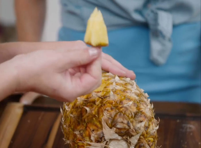 Hand holding a freshly cut pineapple slice over a pineapple, illustrating Meghan Markle kitchen hack concept. Hand holding a freshly cut pineapple slice over a pineapple, illustrating Meghan Markle kitchen hack concept.