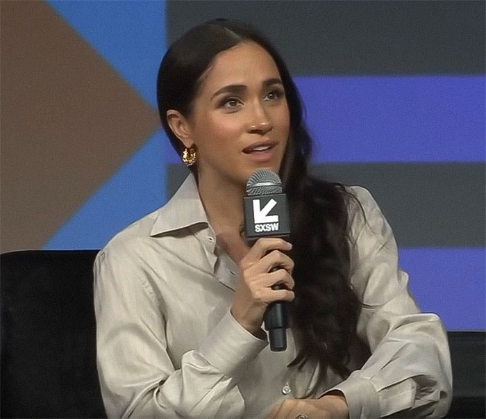 Meghan Markle speaking at SXSW event, holding microphone, wearing beige shirt and gold earrings. Meghan Markle speaking at SXSW event, holding microphone, wearing beige shirt and gold earrings.