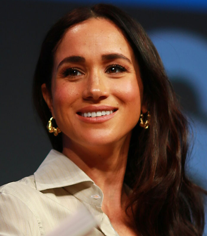 Meghan Markle smiling at an event, showcasing her natural look with loose hair and gold hoop earrings. Meghan Markle smiling at an event, showcasing her natural look with loose hair and gold hoop earrings.
