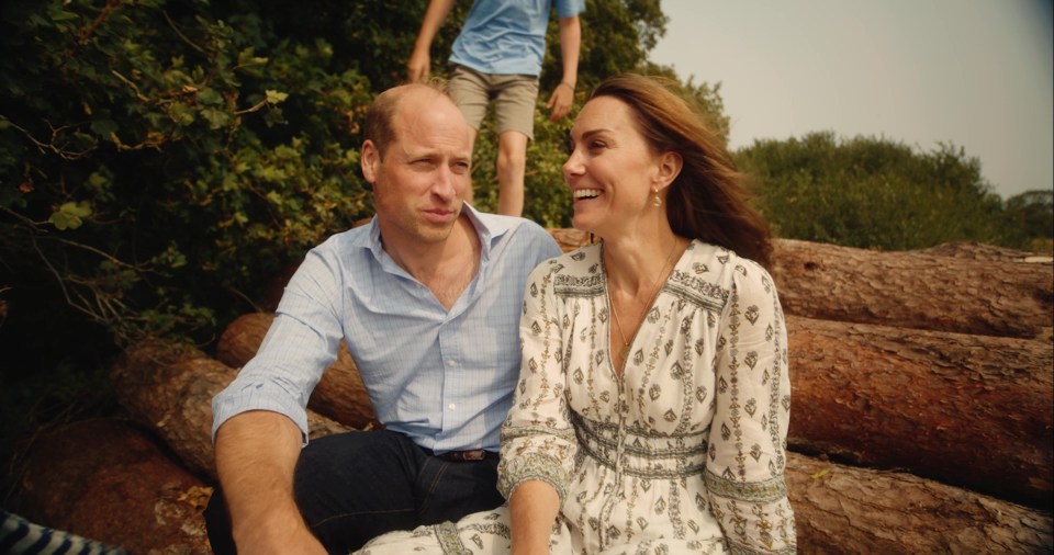 Prince William and Catherine, Princess of Wales, sitting on logs with their son in the background.