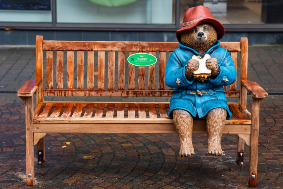 Statue of Paddington Bear sitting on a bench, eating a marmalade sandwich.