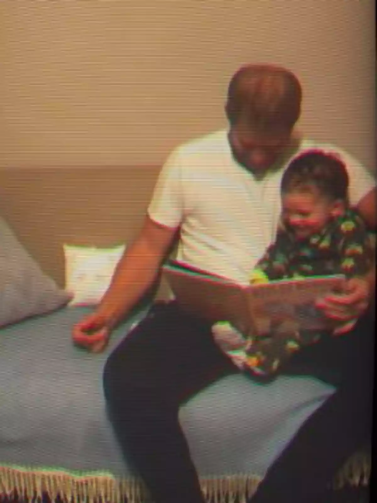 Prince Harry and Archie sitting on a couch reading a book together and smiling