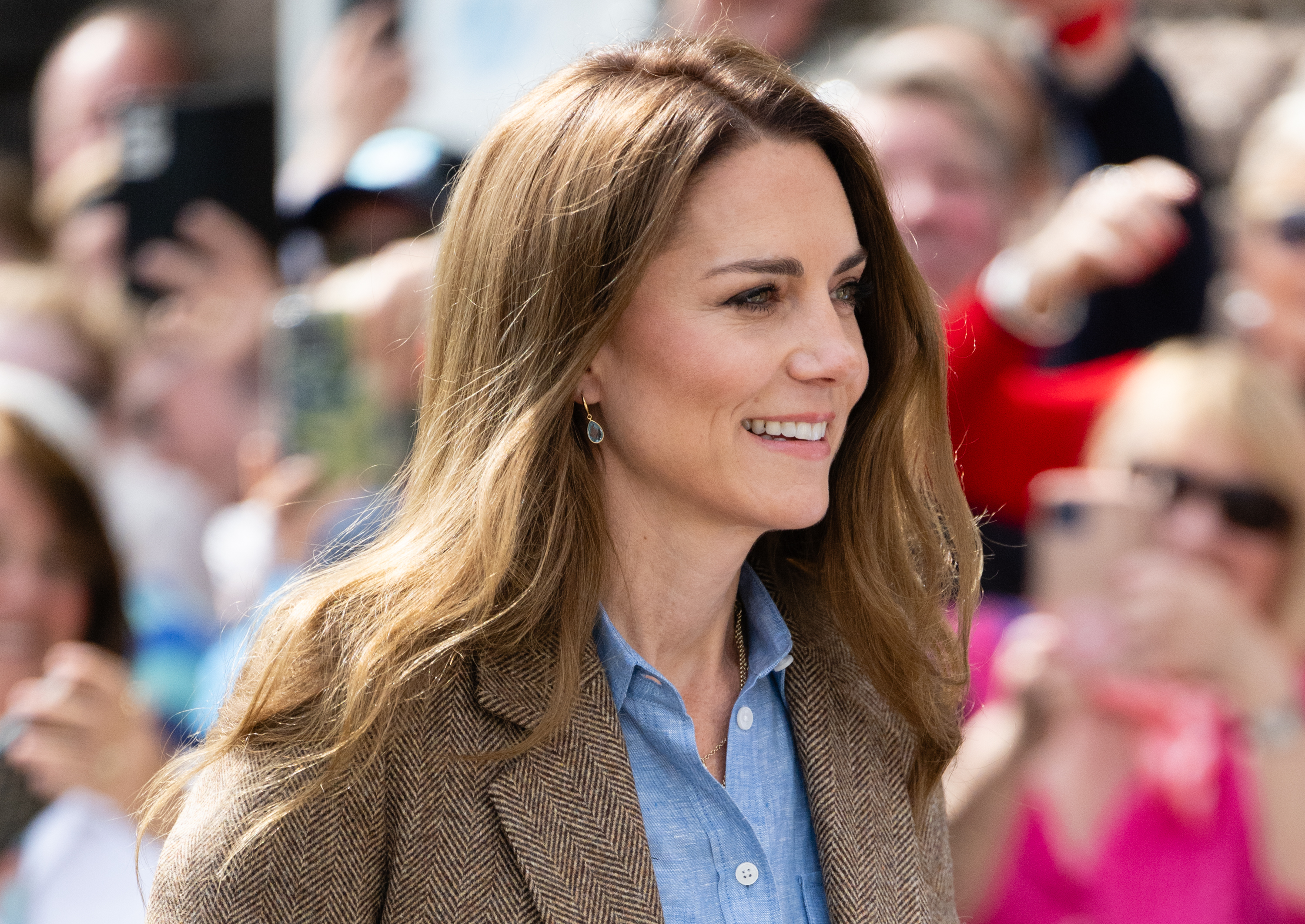 Kate Middleton smiling with a crowd of fans behind her