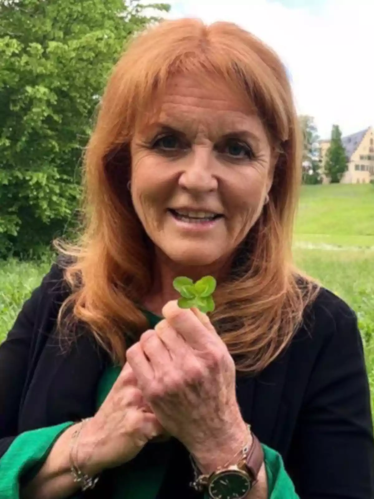 Smiling red-haired woman holds a four-leaf clover in a green field