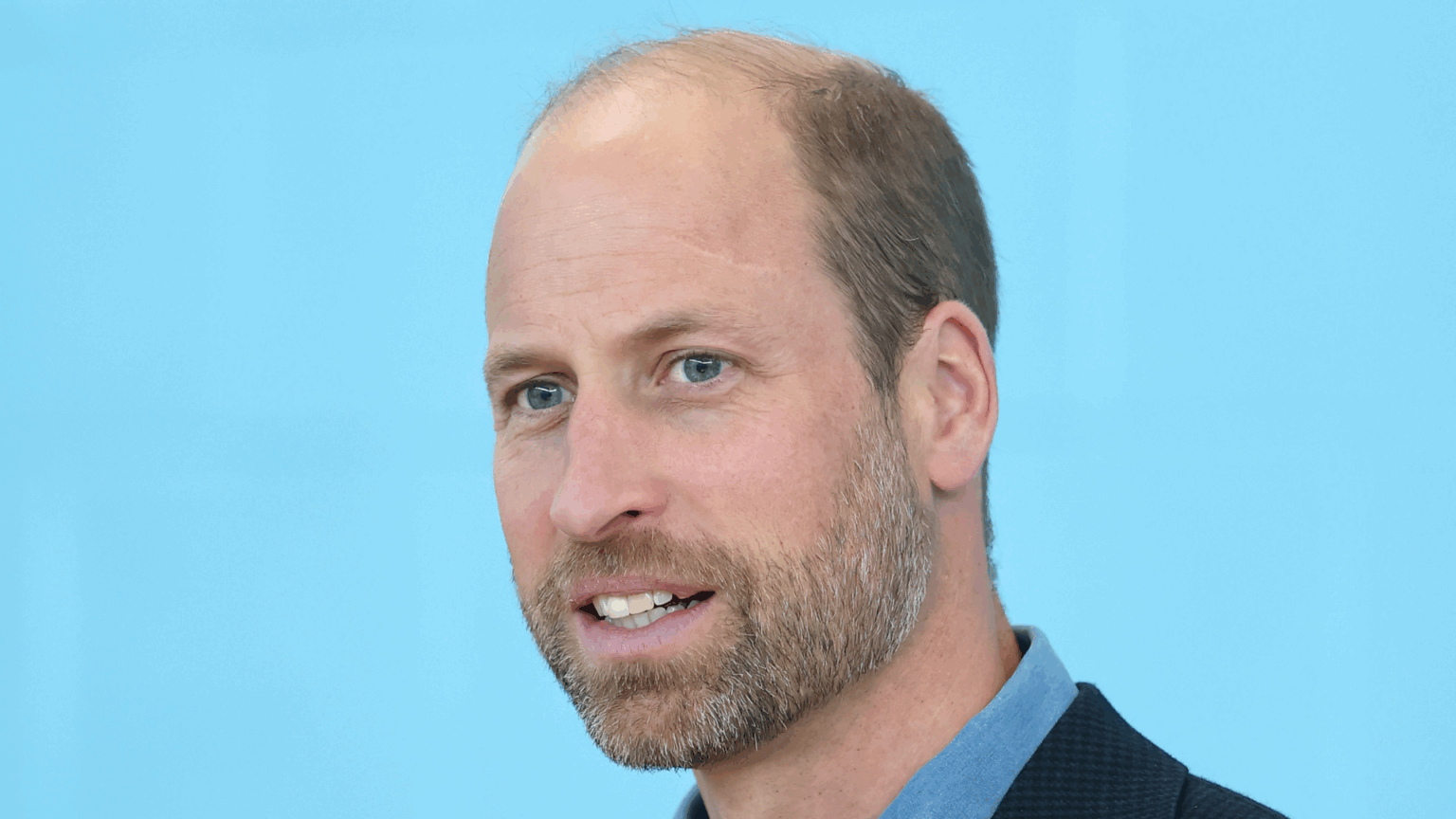 A headshot of Prince William smiling in a blue shirt