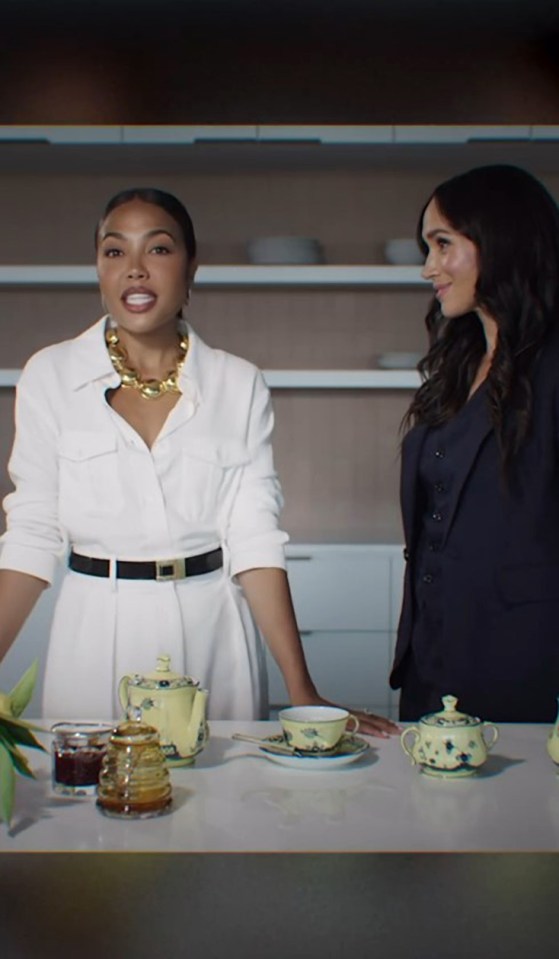 Meghan Markle and a woman in a white dress sit at a table with teacups and a teapot.