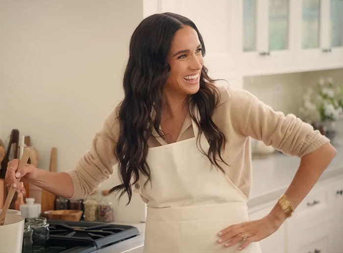 Meghan Markle smiling in a kitchen wearing an apron while sharing her kitchen hack in a bright home setting. Meghan Markle smiling in a kitchen wearing an apron while sharing her kitchen hack in a bright home setting.