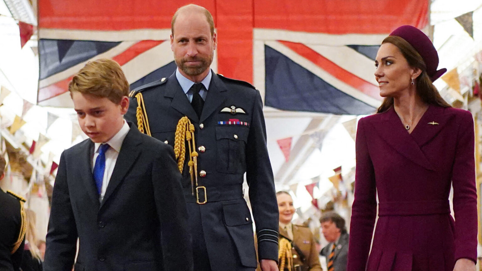 Prince George Following in Dad William’s Footsteps at Eton Kate Middleton looks at Prince William, who is wearing military uniform in front of the British flag, while Prince George walks with his head down
