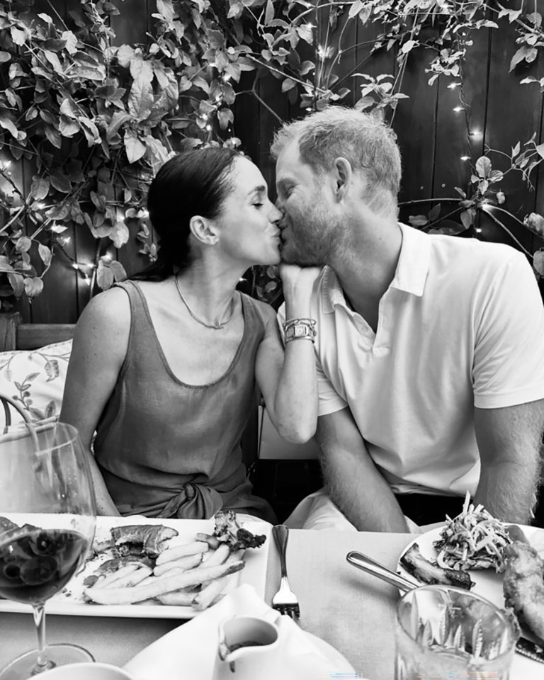 Black and white photo of Prince Harry and Meghan Markle kissing at a table with food.