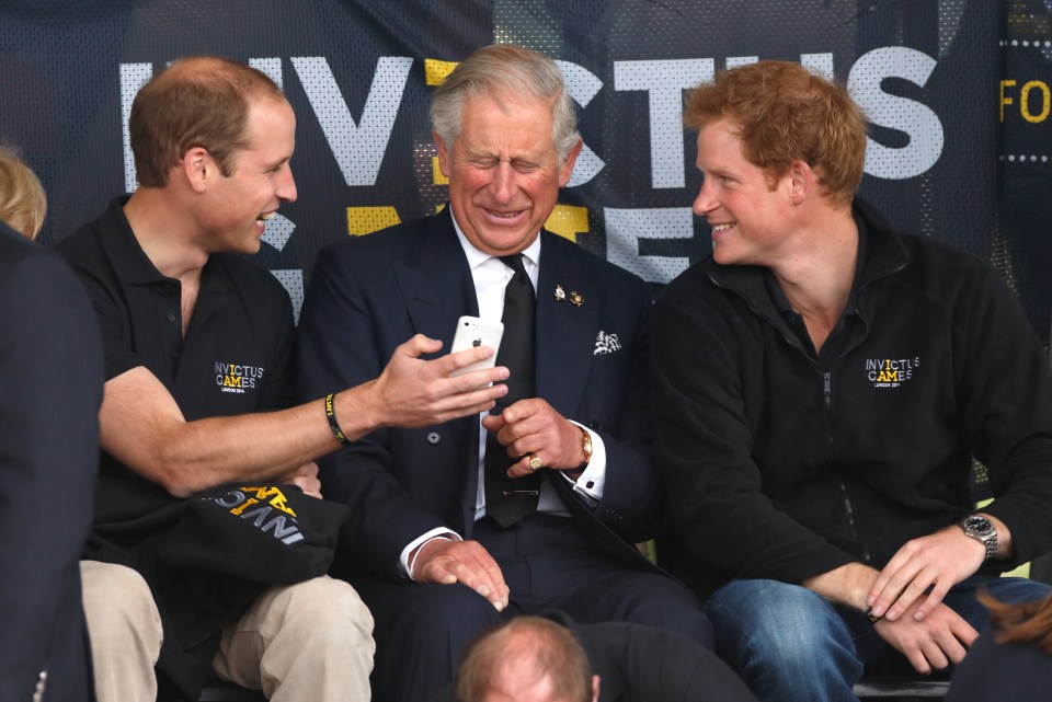 Prince William, Prince Charles, and Prince Harry looking at a mobile phone at the Invictus Games.