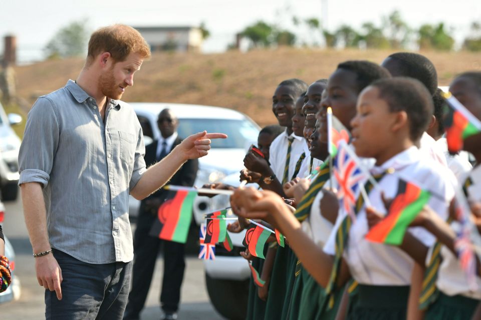 Prince Harry interacting with children holding British and Malawian flags.