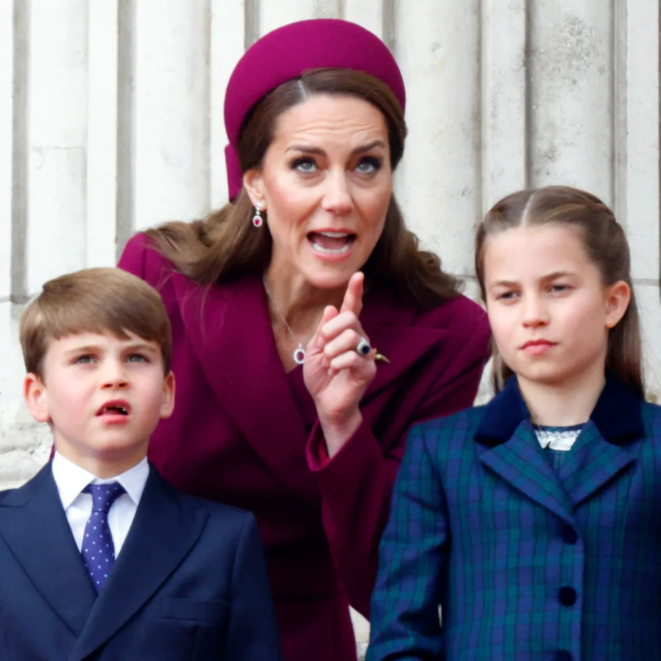 Kate Middleton looks stern while wearing a deep red coat dress and matching hat as she instructs children Prince George, Prince Louis, and Princess Charlotte.