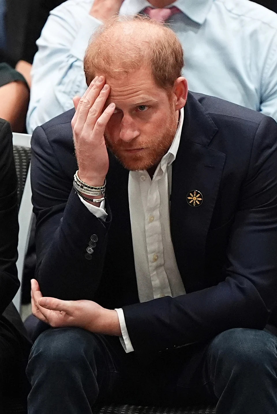 Prince Harry with his head down looking upset in a dark suit.