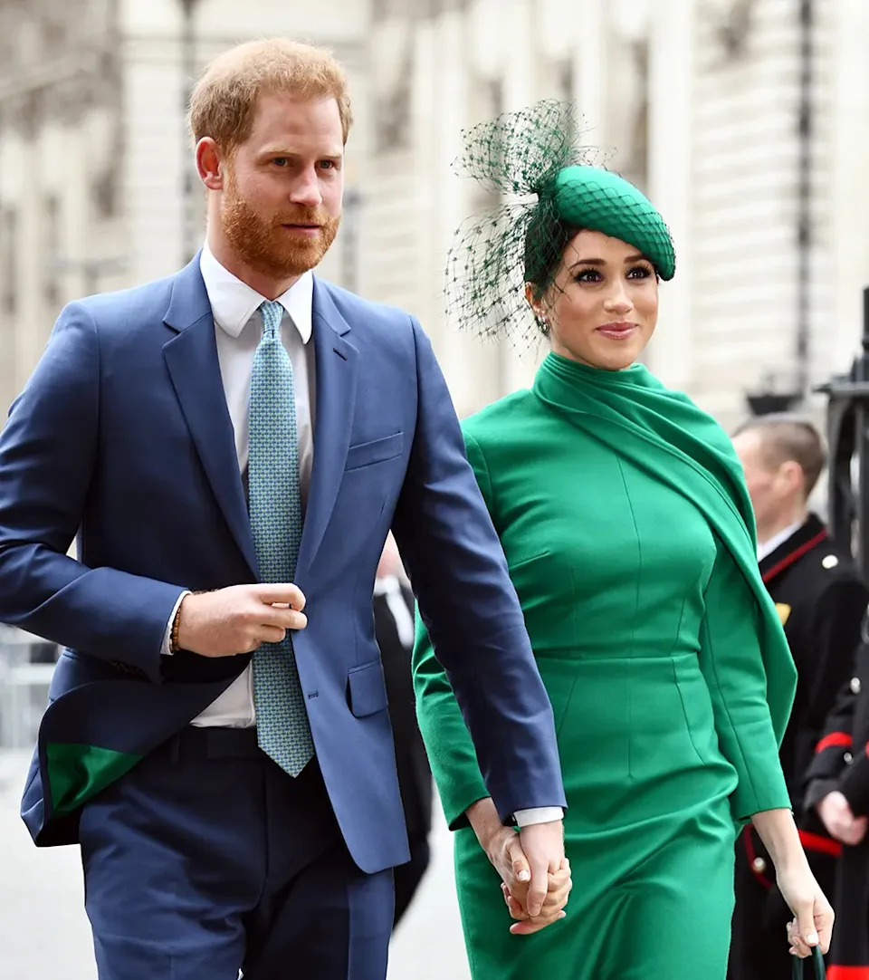 Prince Harry wearing a blue suit walking next to Meghan Markle wearing a bright green dress.