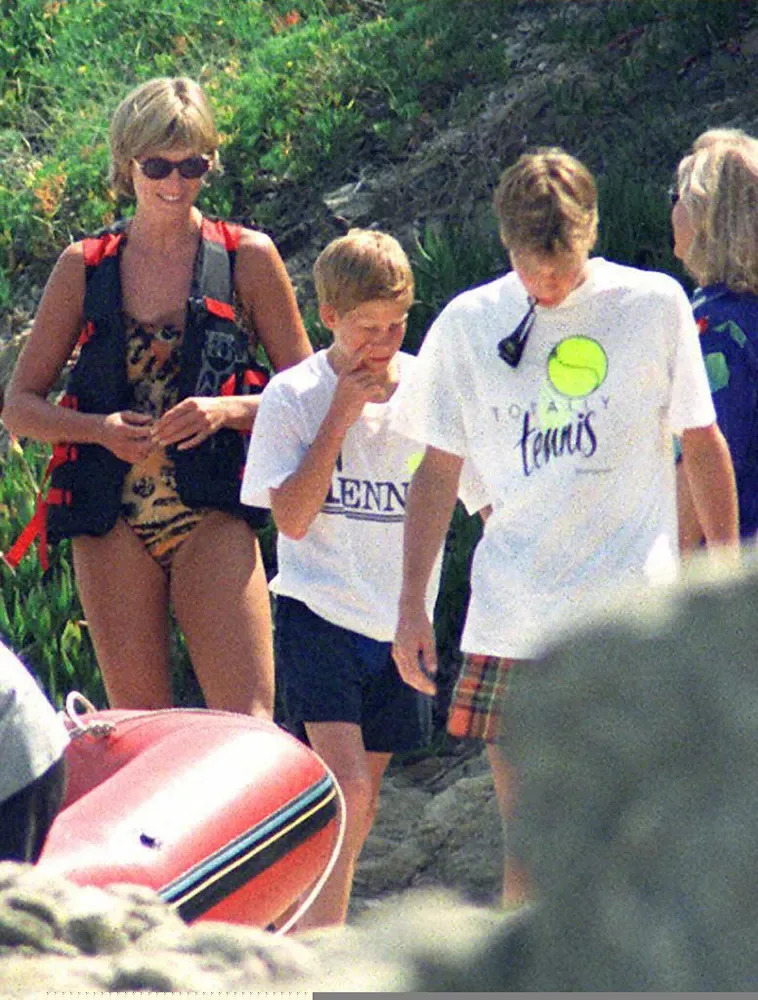 Princess Diana smiling in a leopard swimsuit walking next to Prince Harry and Prince William.