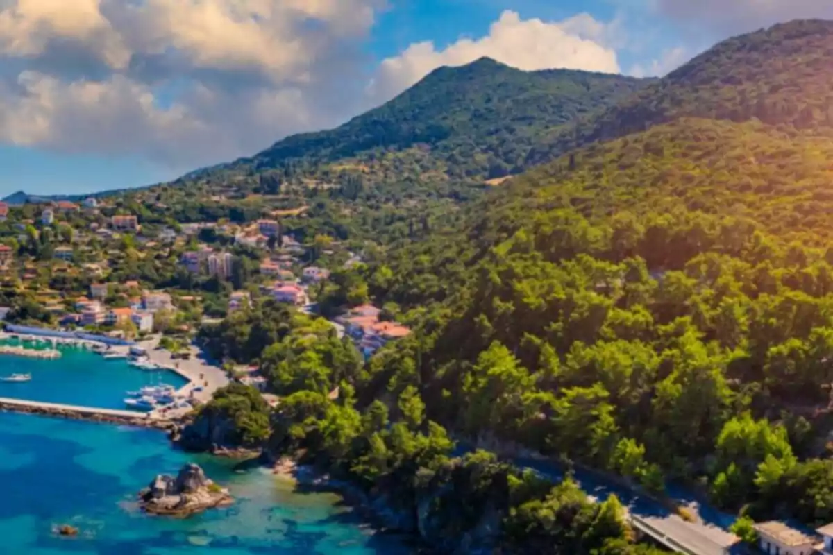 Panoramic view of a coastal town surrounded by green hills and blue sea under a partly cloudy sky