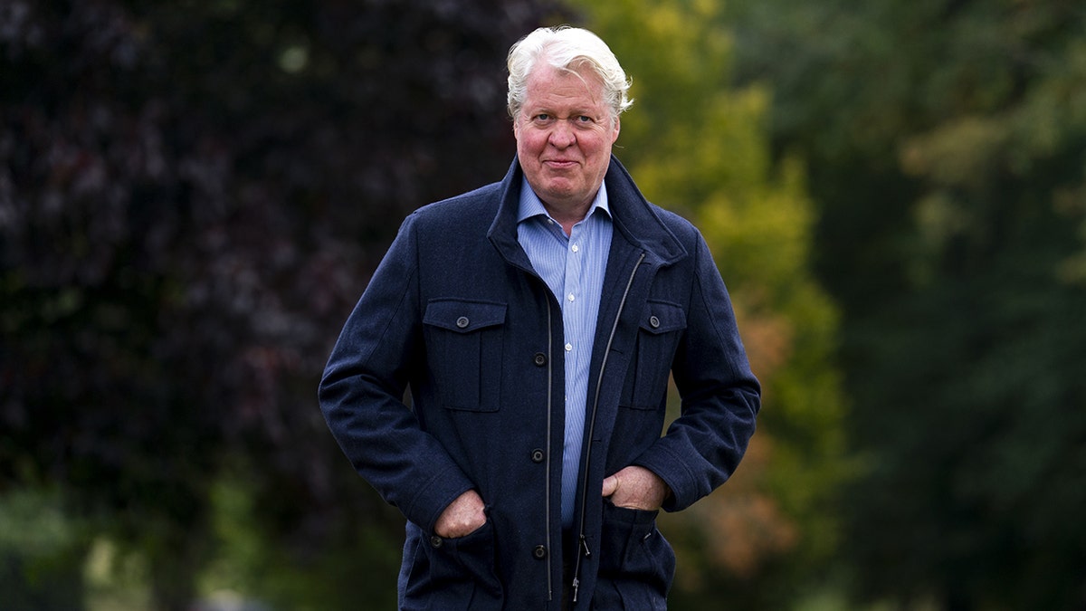 Charles Spencer wearing a dark blue jacket and a white blue shirt smiling with his hands in his pockets.