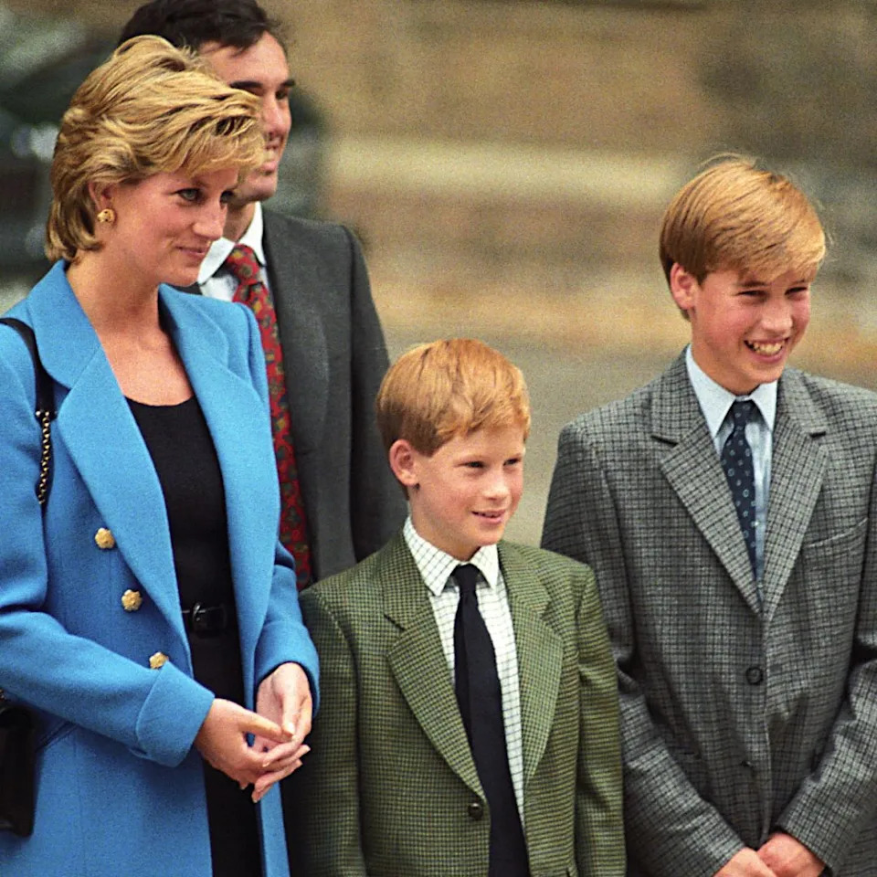 Princess Diana wears a blue suit jacket while posing with young sons Prince Harry and Prince William who wear gray suits during a visit to Eton school.