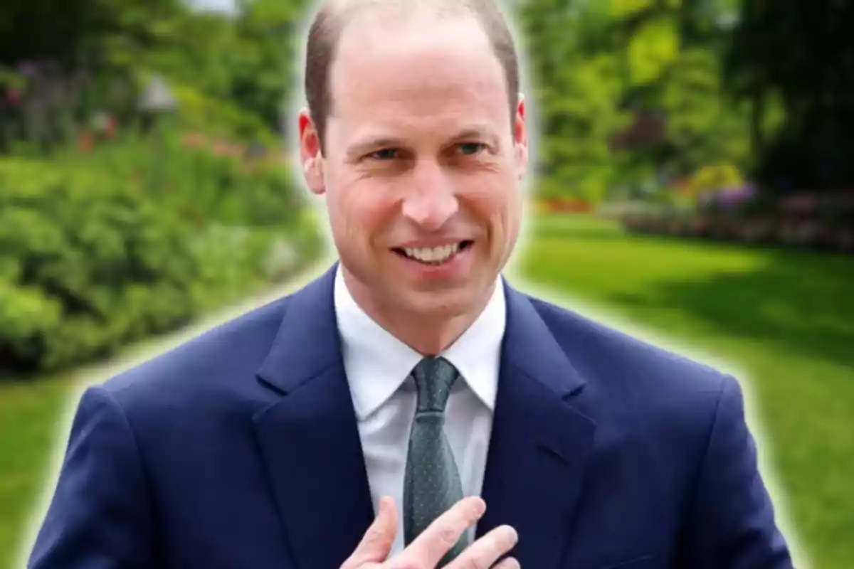 Man in a blue suit and green tie smiling in a garden with greenery in the background