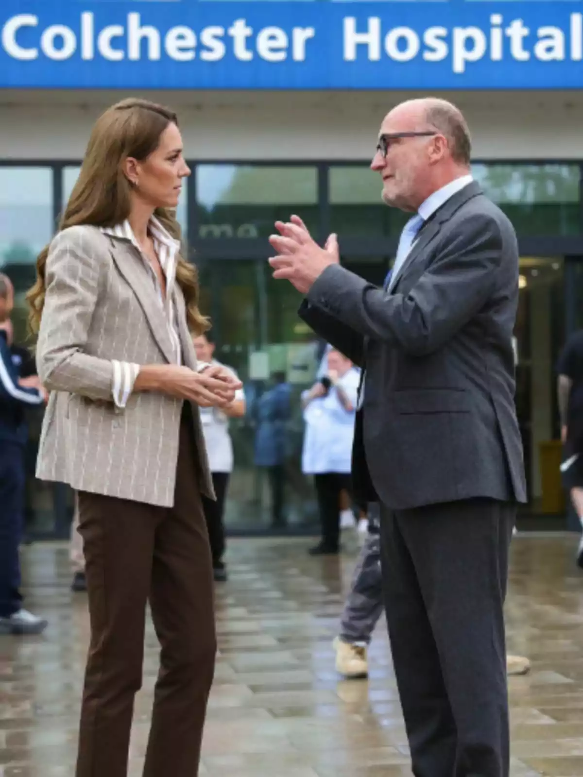 Kate Middleton and a man are talking in front of the entrance to a hospital called Colchester Hospital.