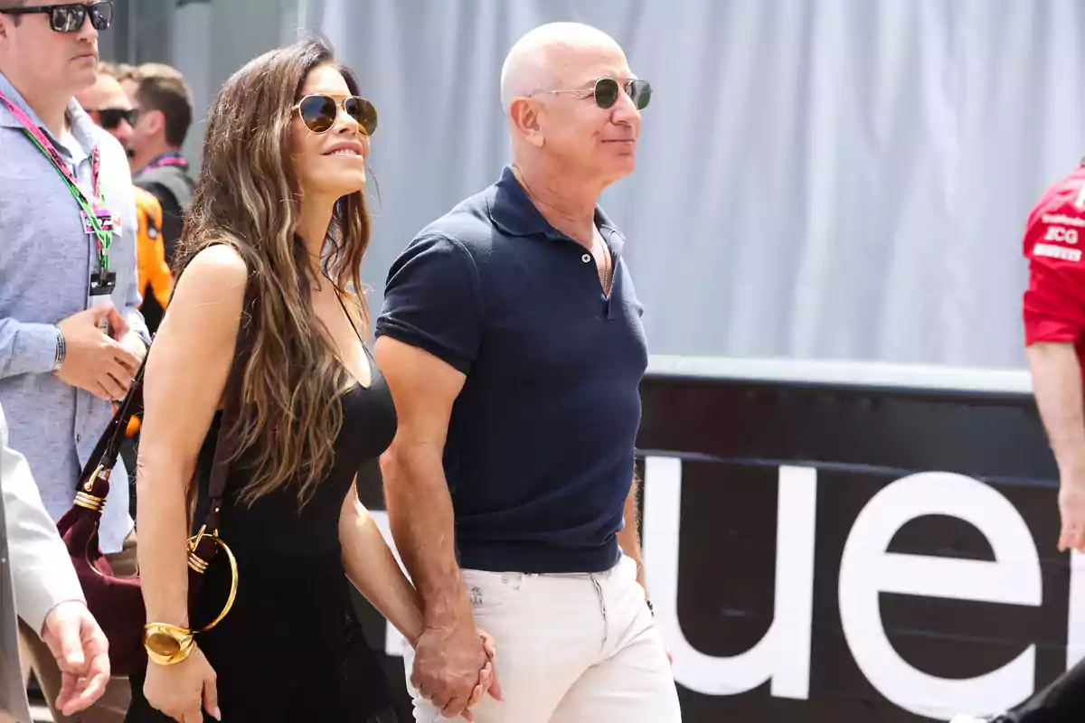 Lauren Sánchez and Jeff Bezos walking hand in hand outdoors, both wearing sunglasses and casual clothes Lauren Sánchez and Jeff Bezos walking hand in hand outdoors, both wearing sunglasses and casual clothes