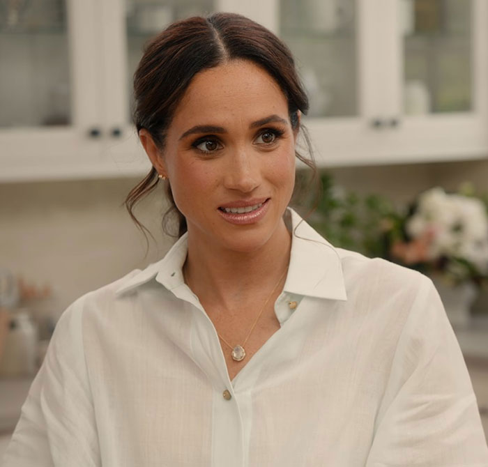 Meghan Markle in a white blouse indoors, reacting to accusations related to an embarrassing fruit-picking photo controversy. Meghan Markle in a white blouse indoors, reacting to accusations related to an embarrassing fruit-picking photo controversy.