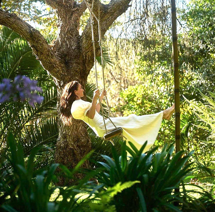 Meghan Markle on a swing in a garden setting, surrounded by greenery, linked to fruit-picking photo controversy. Meghan Markle on a swing in a garden setting, surrounded by greenery, linked to fruit-picking photo controversy.