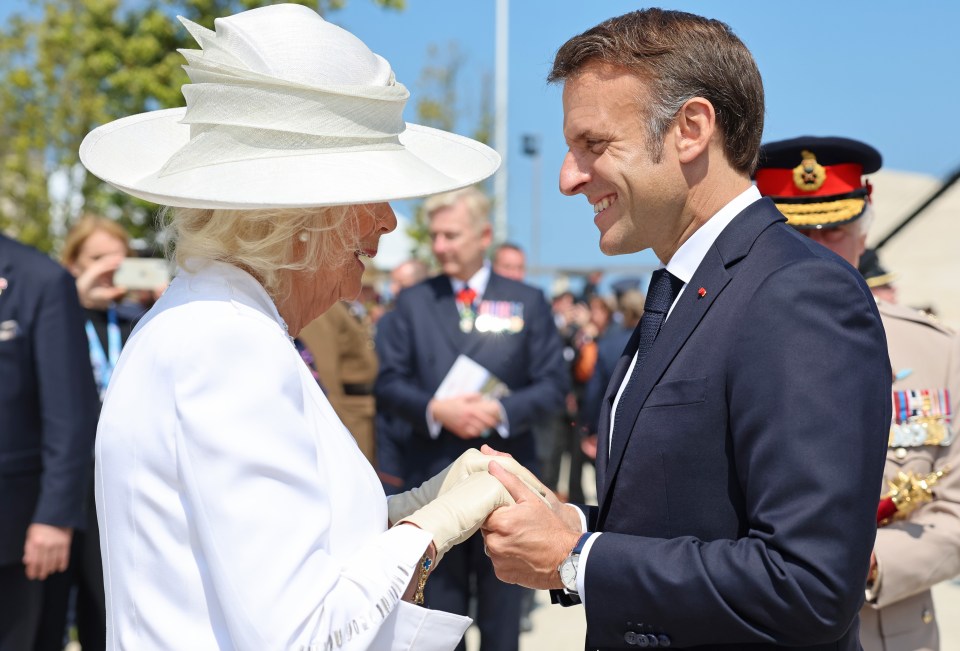 Queen Camilla and President Emmanuel Macron shaking hands at a commemorative event.