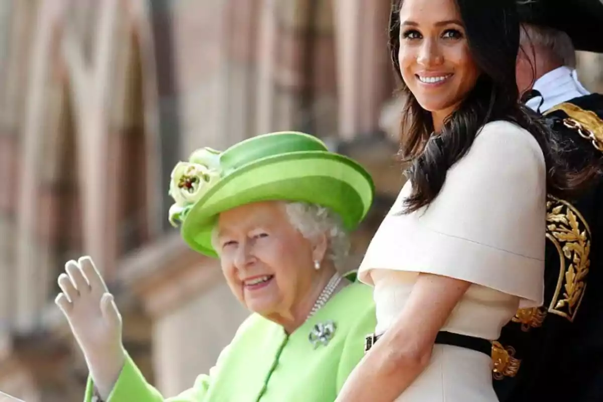 Two women smile at a formal event; one is wearing a green outfit with a matching hat, and the other is dressed in white. Two women smile at a formal event; one is wearing a green outfit with a matching hat, and the other is dressed in white.