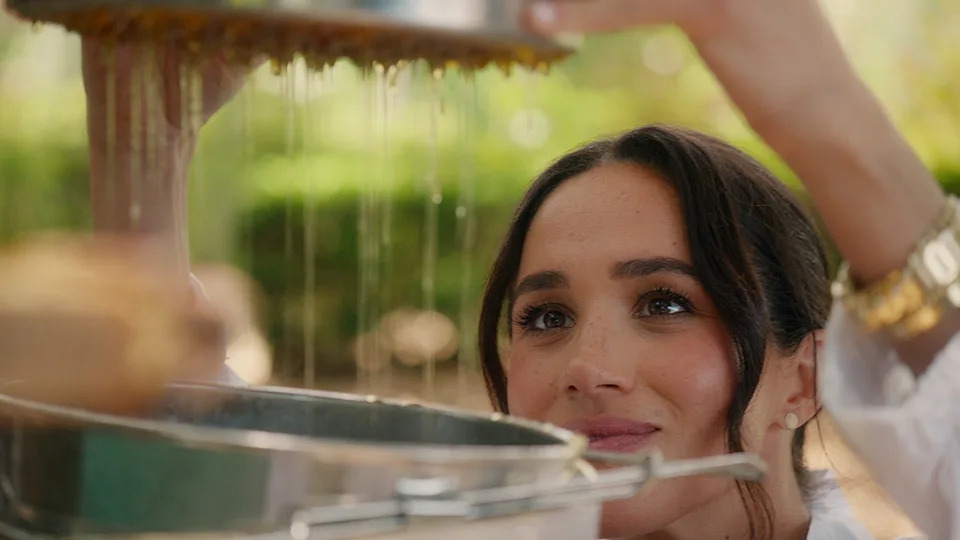 A close-up of Meghan Markle handling honey in a backyard.