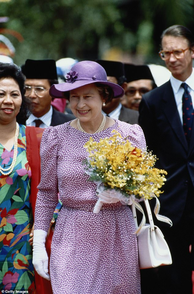 Queen Elizabeth II, carrying a bouquet of flowers and her Private Secretary, Sir Robert Fellowes (to the right of the image) during a state visit to Malaysia, in October 1989