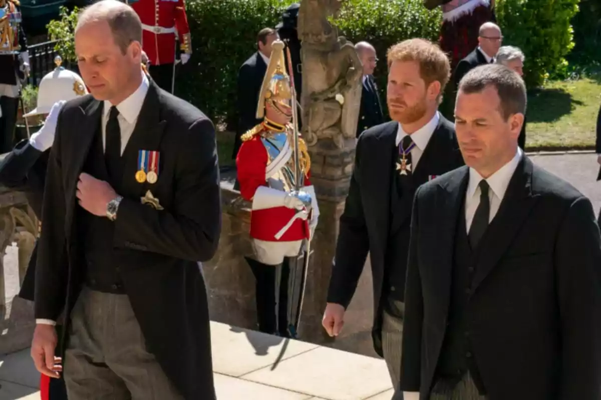 Princes William and Harry and Peter Phillips, dressed in formal suits, walk together at a solemn outdoor event while a guard in ceremonial uniform stands in the background.