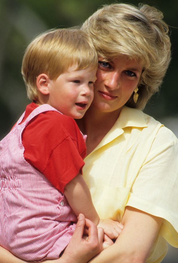 Princess Diana, in a yellow top, holding her son Prince Harry, in a red top and striped dungarees.