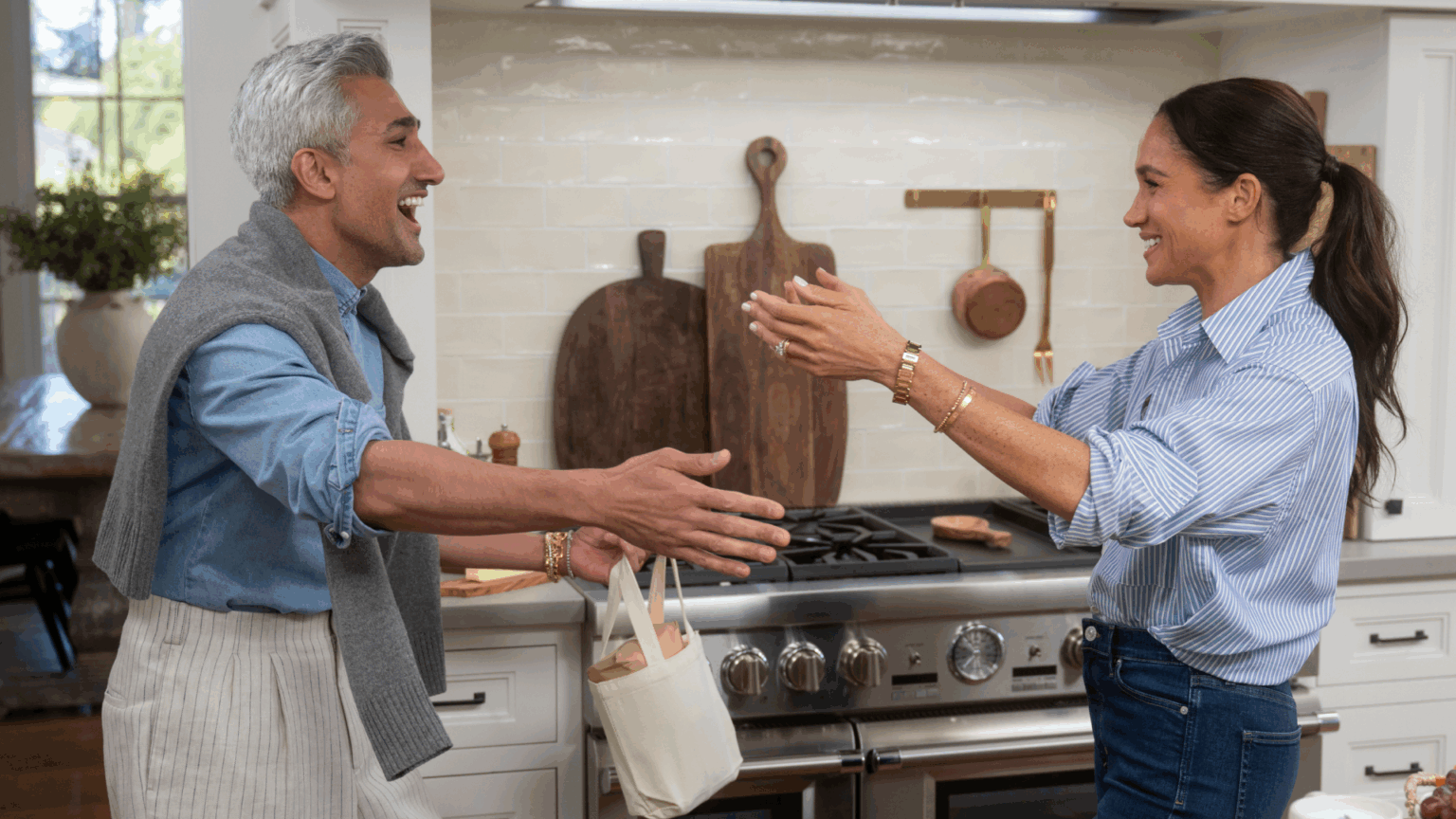 Meghan Markle putting her arms out to hug Tan France in a kitchen