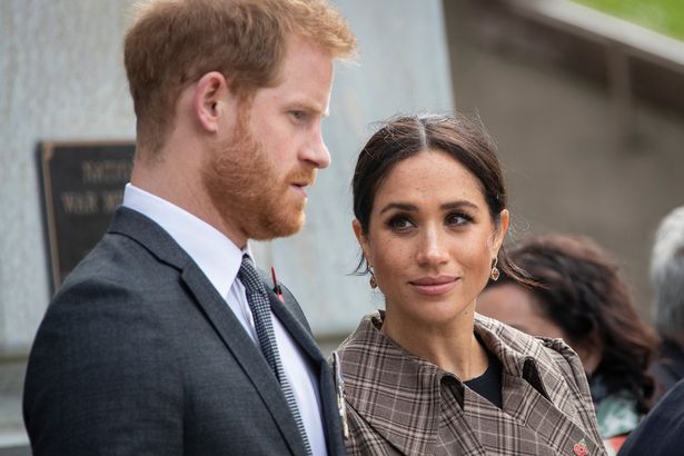 Prince Harry in a grey suit next to Meghan Markle in a checkered jacket.