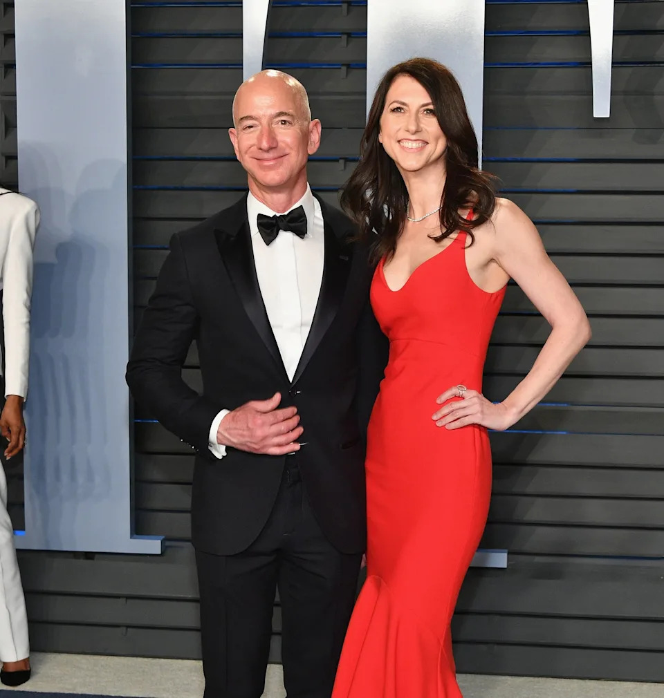 Two people on a red carpet, one in a black tuxedo with a bow tie and the other in a long, sleek red gown with a flared bottom