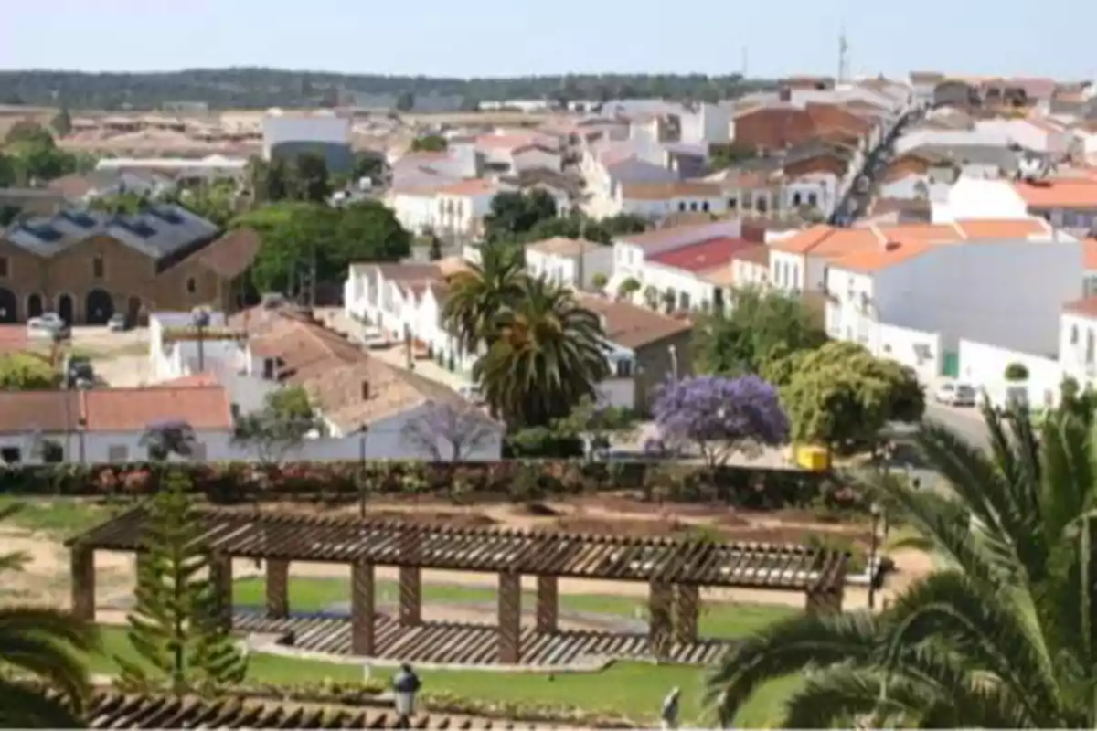 Panoramic view of a village with red-roofed houses, trees, and a park with wooden pergolas in the foreground